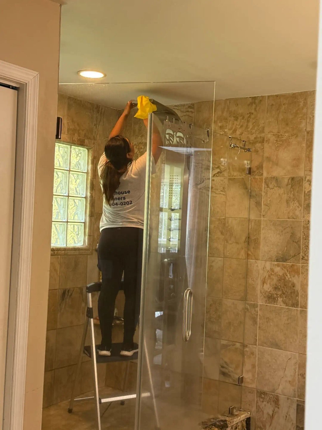 A cleaner wiping a glass shower door in a tiled bathroom