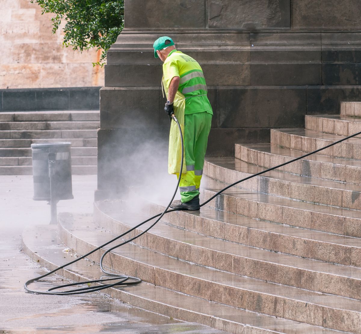 A worker pressure washing stone stairs outdoors