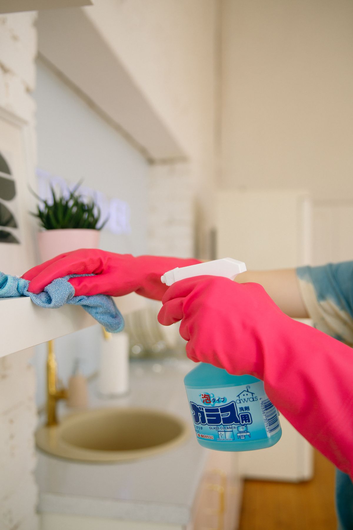 Gloved hands spraying and wiping a bathroom counter