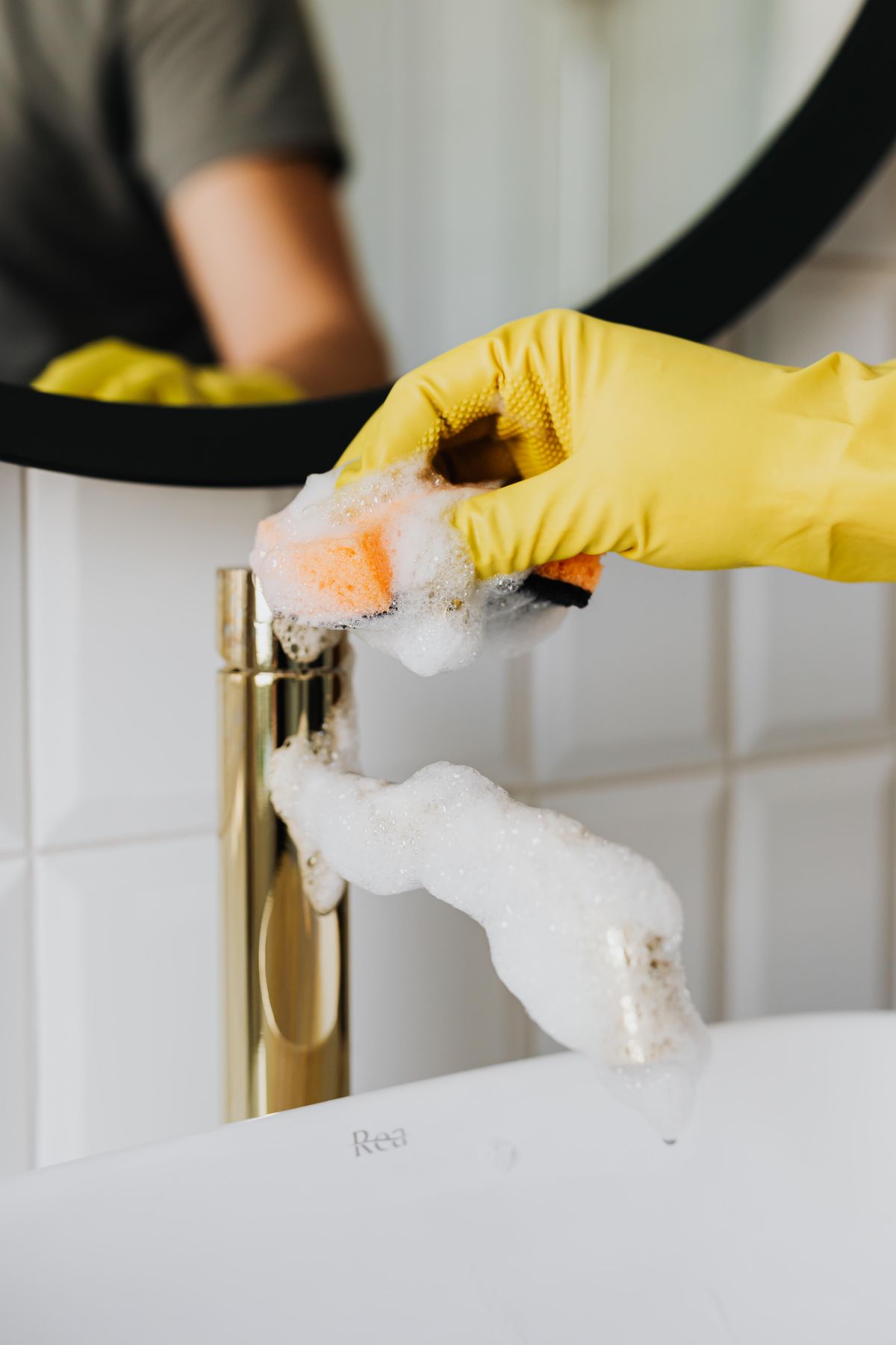 A gloved hand scrubbing a gold faucet and sink