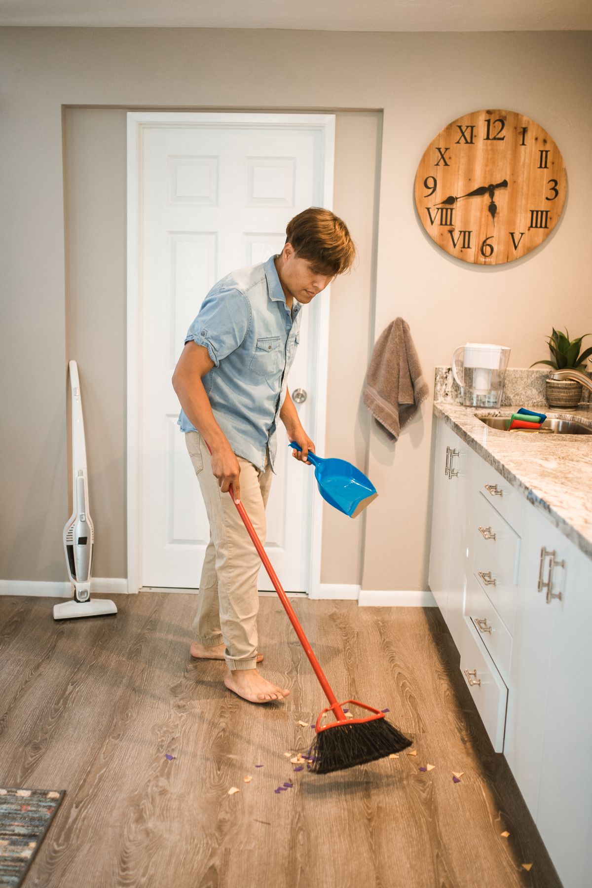 A man sweeping a kitchen floor with a broom and dustpan