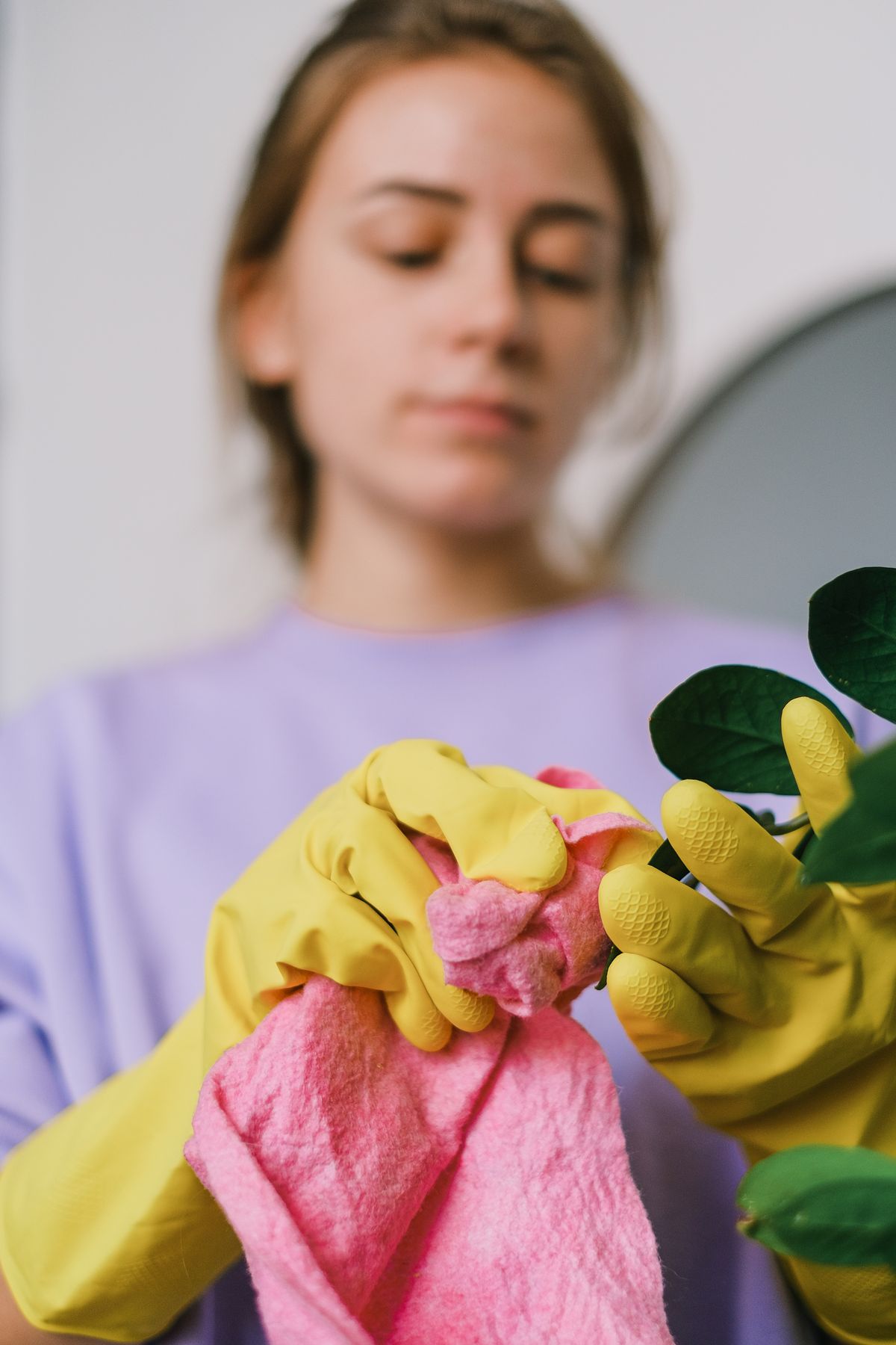 A cleaner in yellow gloves holding a pink cleaning cloth